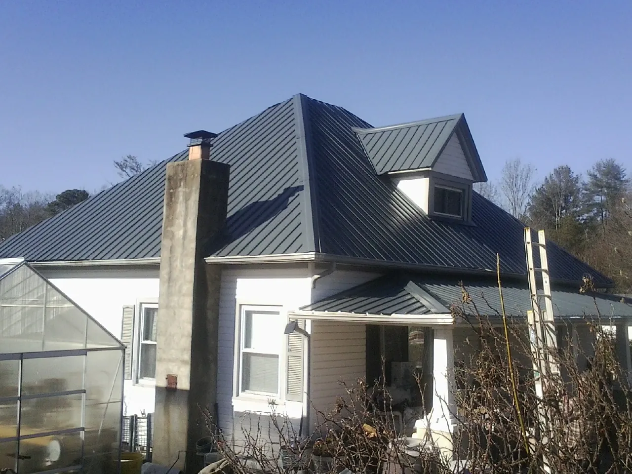 Dark blue standing seam metal roof on a white farmhouse with dormer — Slate & Tile Roof Repair by Roofing Brothers in Melstone