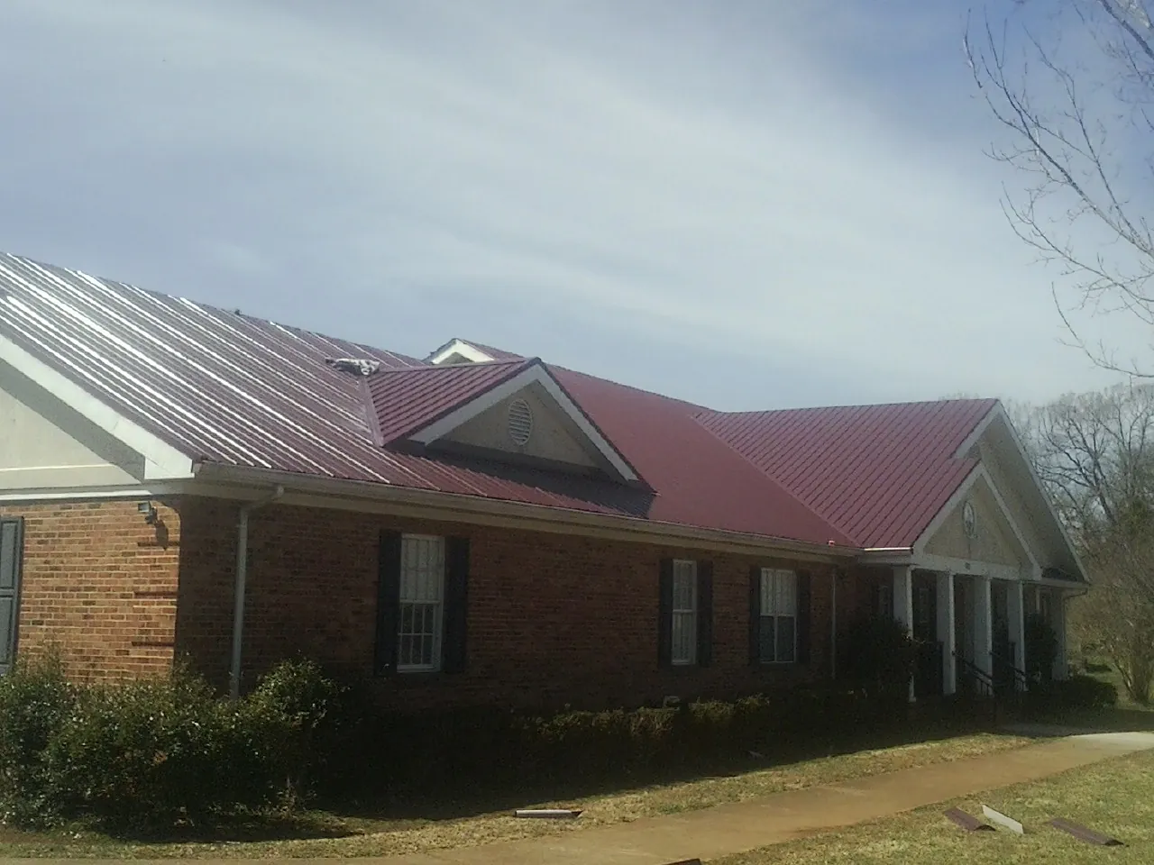 Red metal roof with gabled entries on a long brick building, from a Hail Damage Roof Repair job in Melstone