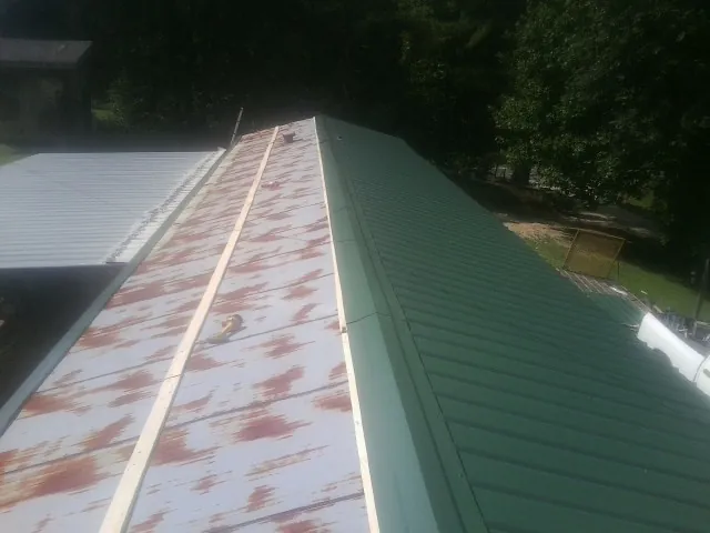 Old rusted panels beside newly installed green metal roofing — Wind Damage Roof Repair by Roofing Brothers in Melstone