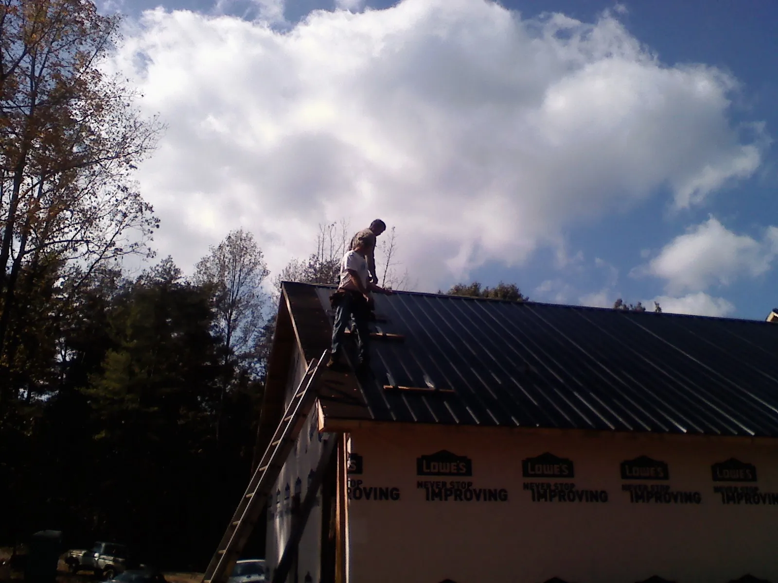 Roofer fastening dark metal panels high against a cloudy sky, from a Roof Inspection job in Melstone
