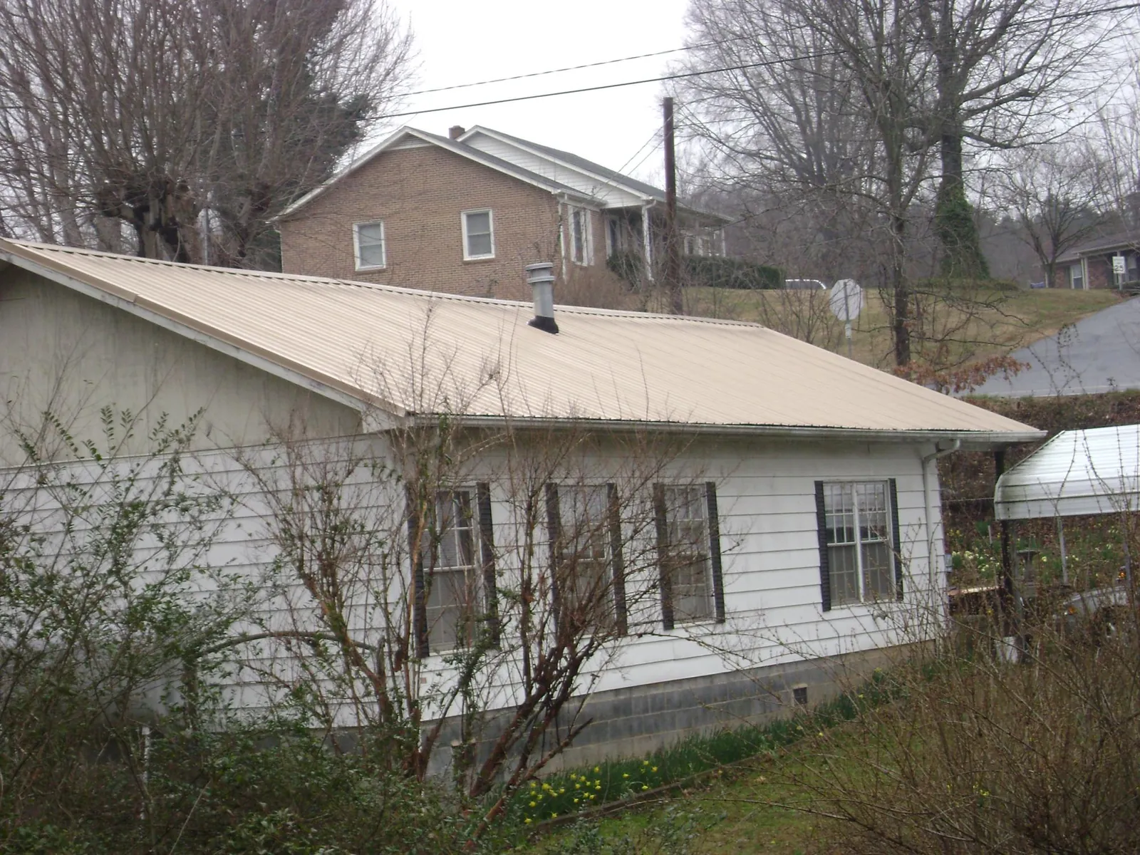 Tan metal roof on a white sided house set into a hillside — Commercial Roofing by Roofing Brothers in Melstone