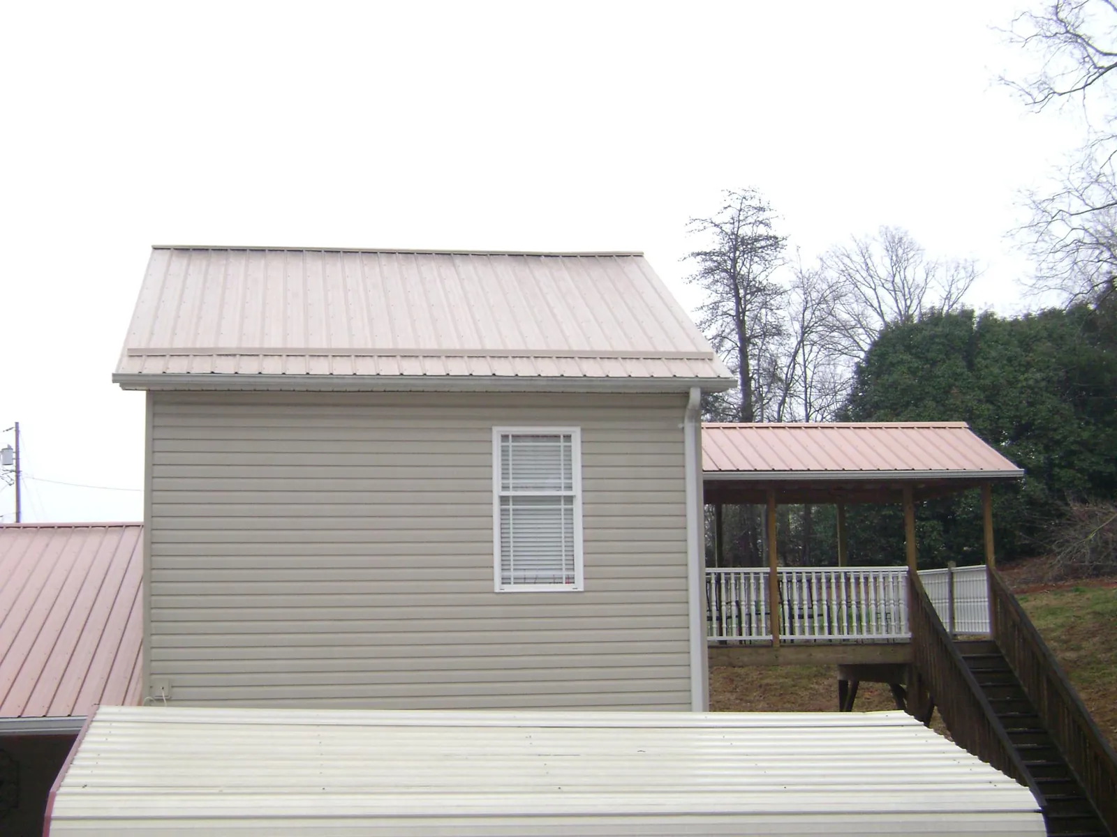 Tan metal roofs on a two story addition and attached porch, from a Roof Replacement job in Melstone